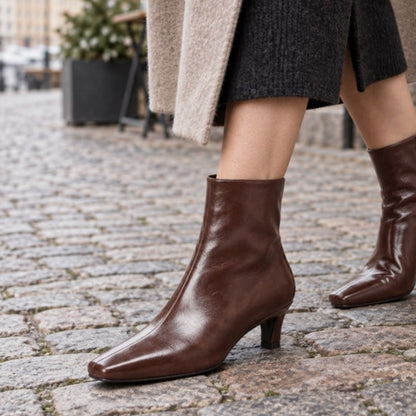 Bruna damankelboots med låg klack, sidovy på stenlagd gata