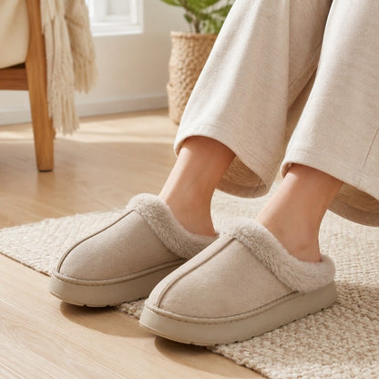 Tofflor, slip-on, ljusbruna med fuskpäls, på fot med ljusa byxor.